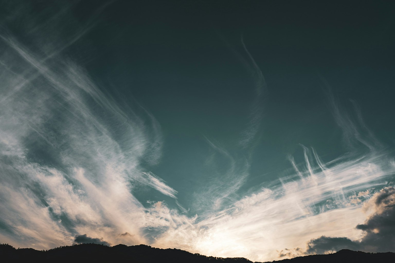 Swirling clouds in a blue sky with mountain silhouette