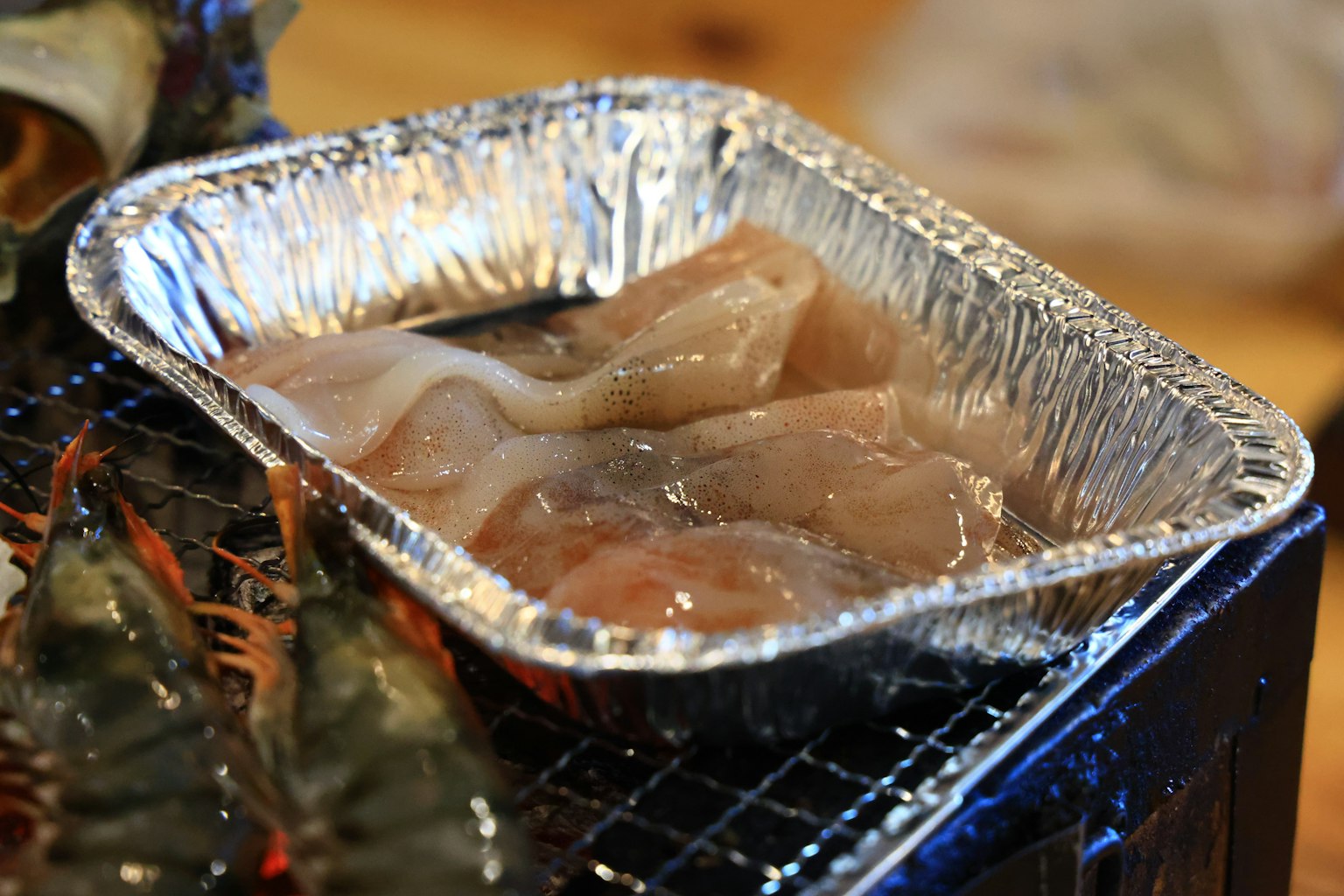 Rohe Garnelen in einer Aluminiumplatte auf einem Grill mit gekochten Lebensmitteln