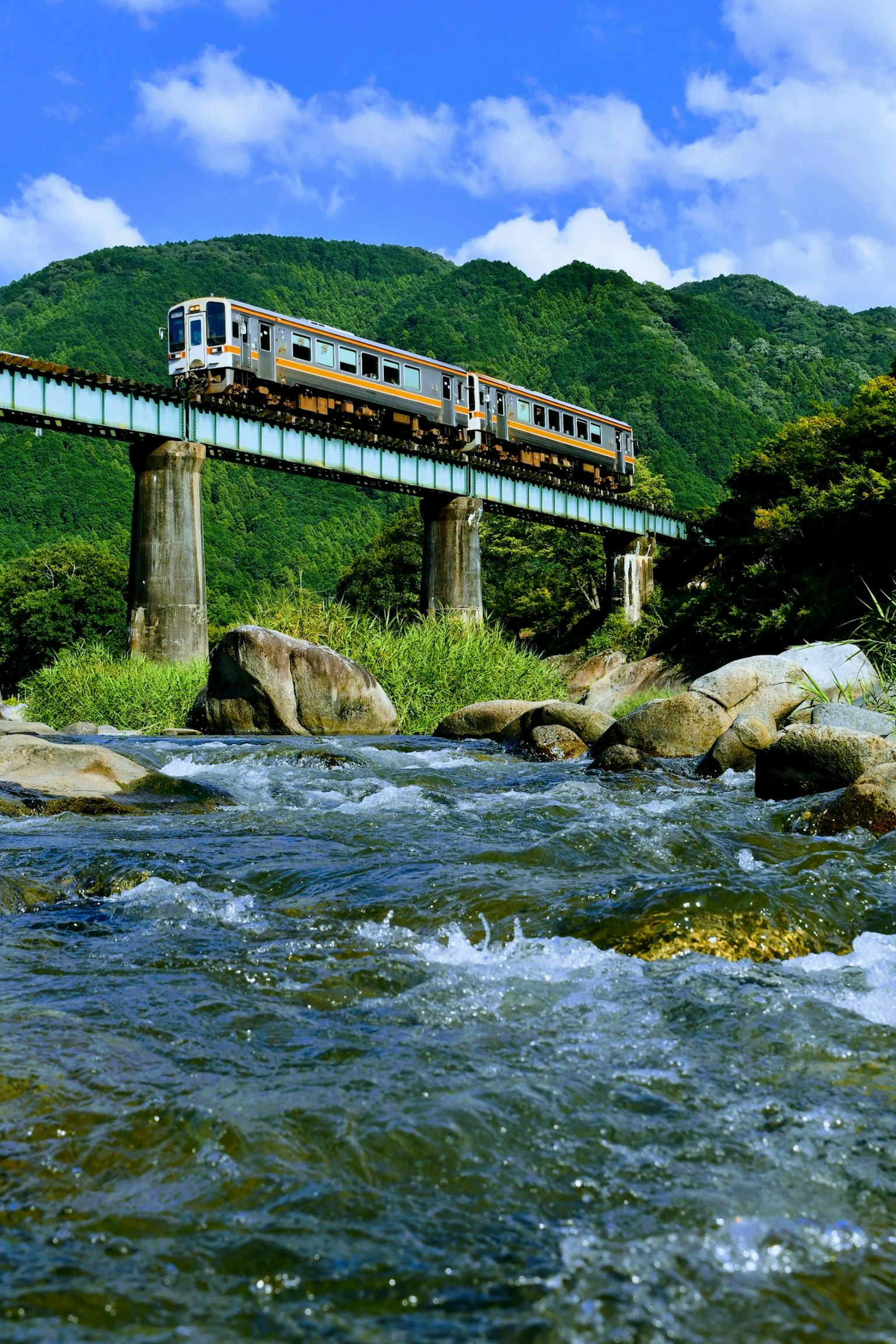 Sebuah kereta melintasi jembatan dengan latar belakang pegunungan dan sungai