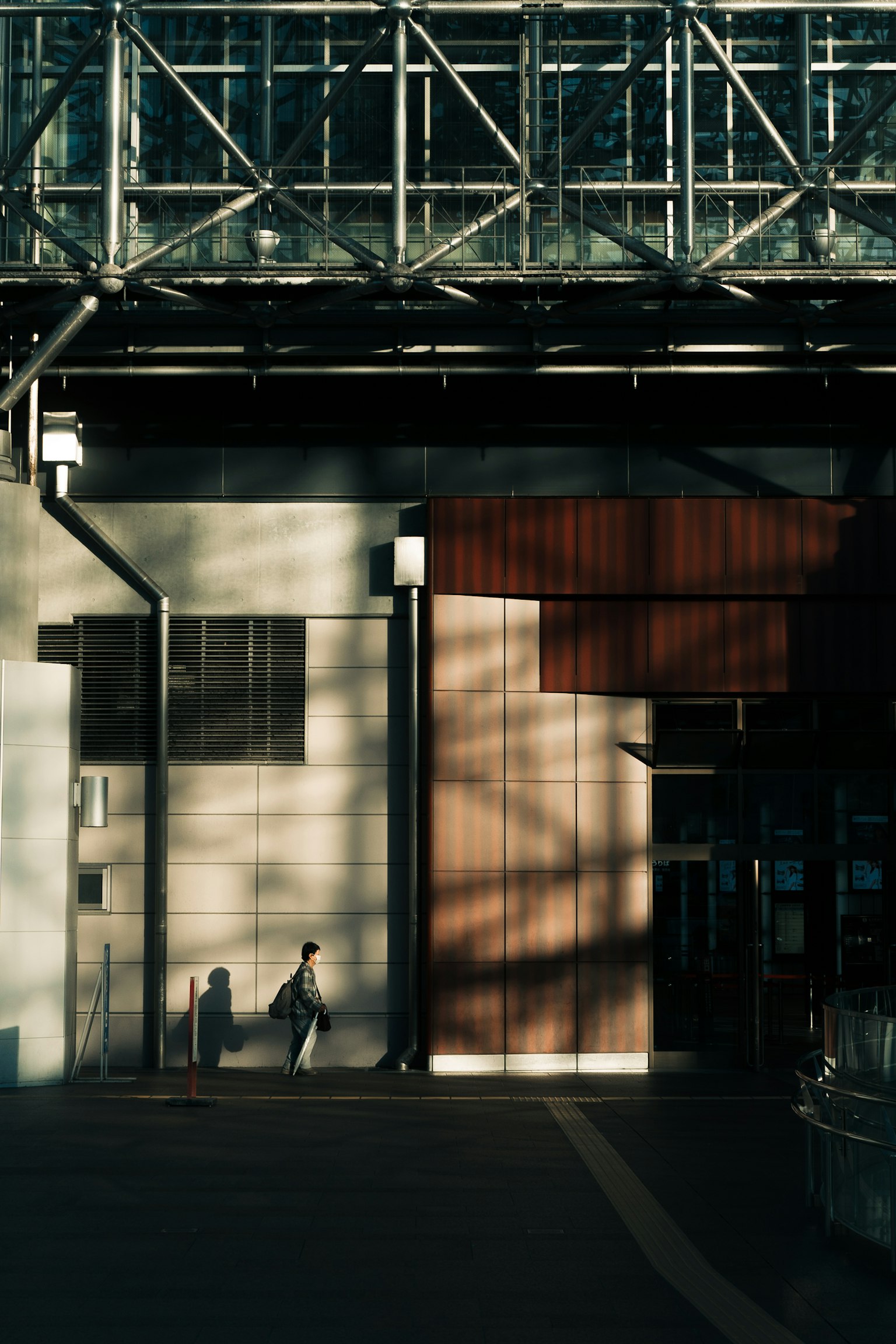 Une personne marchant devant un bâtiment moderne avec des ombres et des éléments structurels