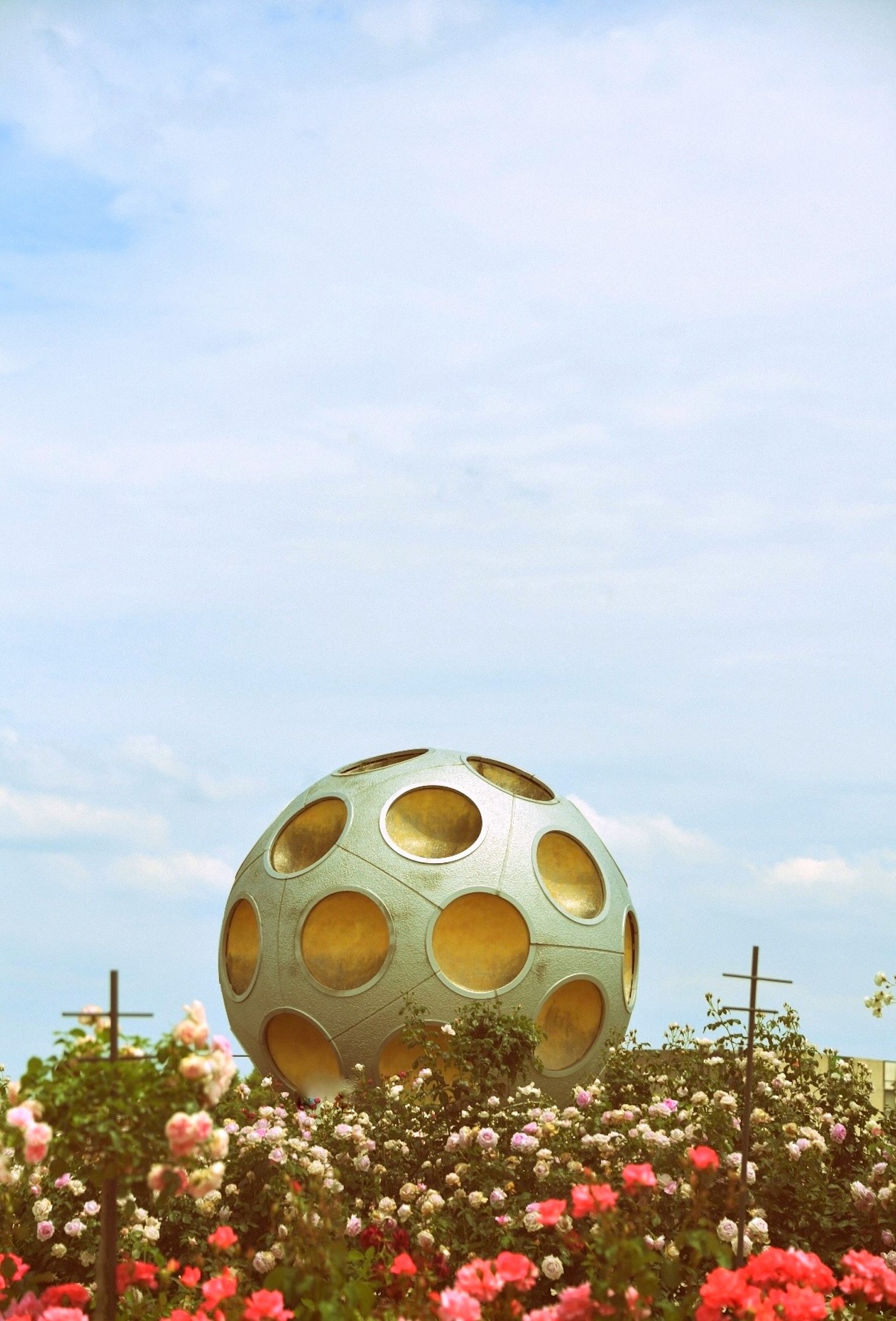 Sculpture sphérique bleue avec des trous entourée de roses colorées