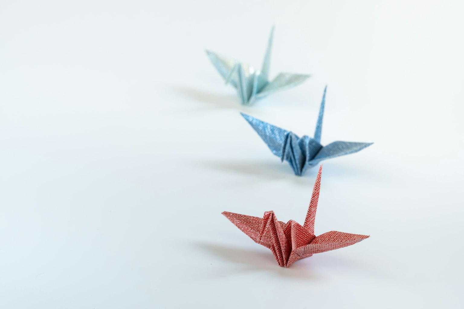 Trois grues en origami bleues et rouges disposées sur un fond simple