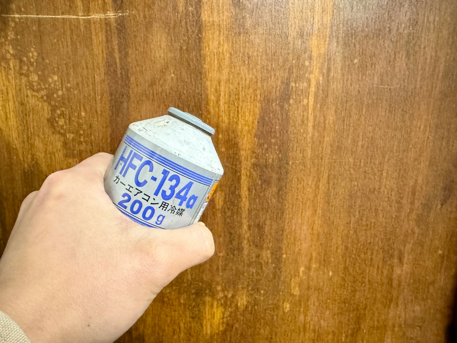 Hand holding an HFC-134a gas can against a wooden background