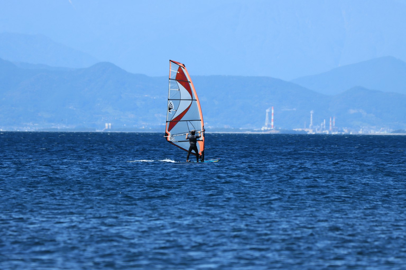 Una persona practicando windsurf en un océano azul con montañas distantes