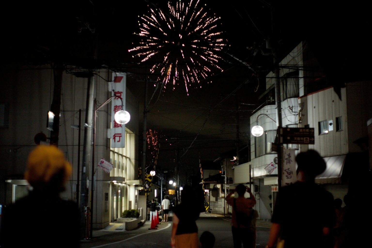 夜空に花火が打ち上げられ人々が見上げる街の風景