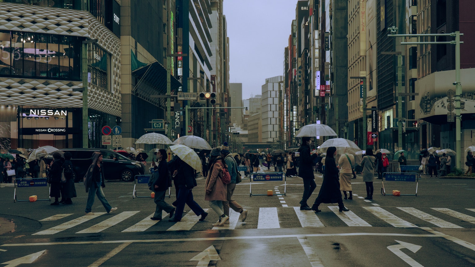 Menschen überqueren die Straße mit Regenschirmen in einer Stadtlandschaft