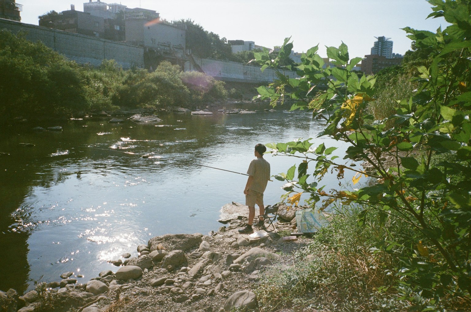 川で釣りをする人の後ろ姿 緑の植物と都市の背景