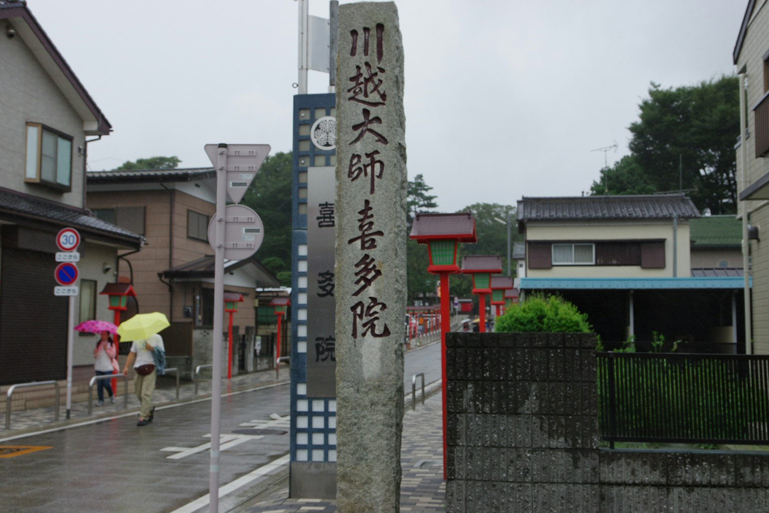 Un monumento in pietra per Kawasu Daishi all'angolo di una strada in un giorno di pioggia