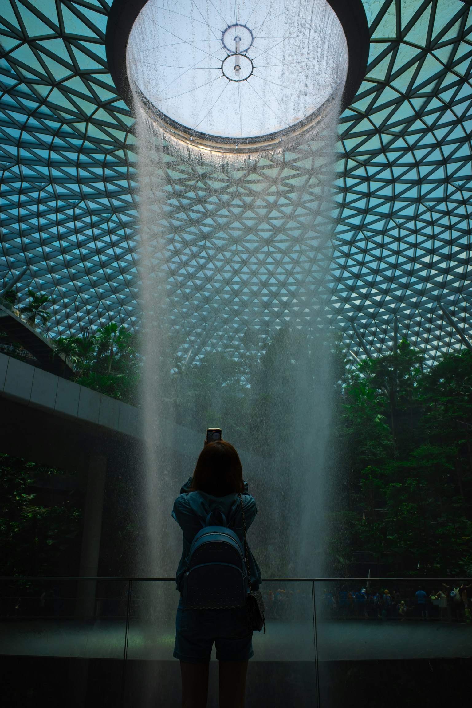 ผู้เข้าชมถ่ายภาพที่สนามบิน Jewel Changi โดยมีน้ำตกและการออกแบบสถาปัตยกรรมที่เป็นเอกลักษณ์
