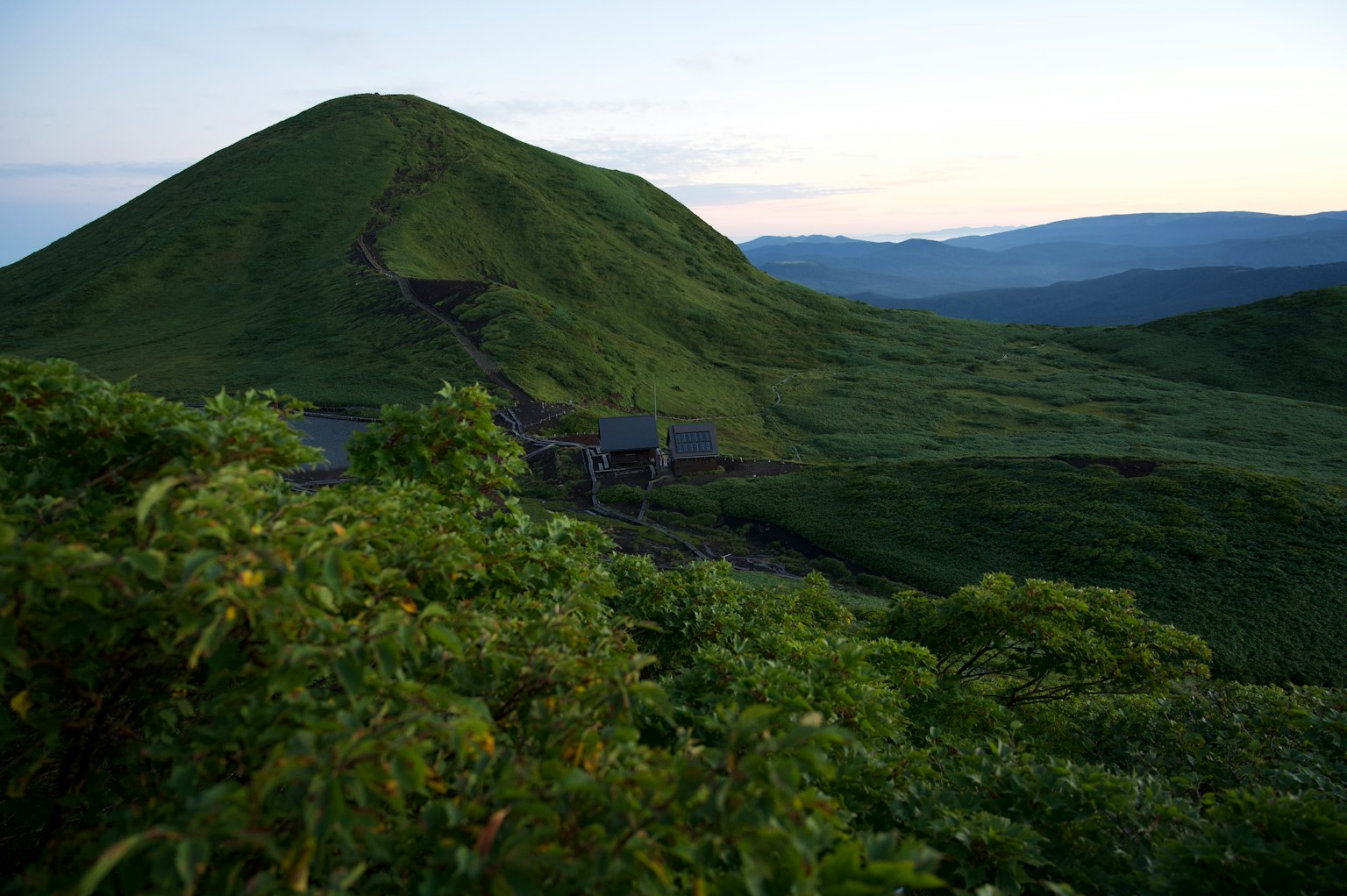 Perbukitan hijau subur dan gunung di bawah langit senja yang tenang