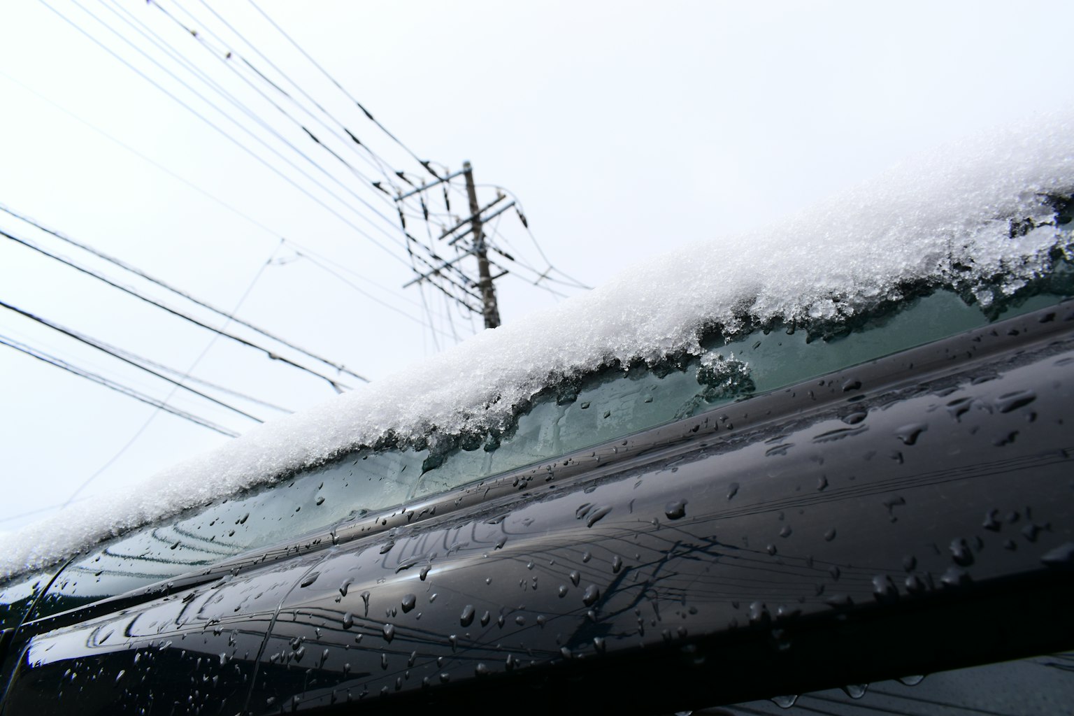 Snow accumulated on the edge of a roof with water droplets on glass