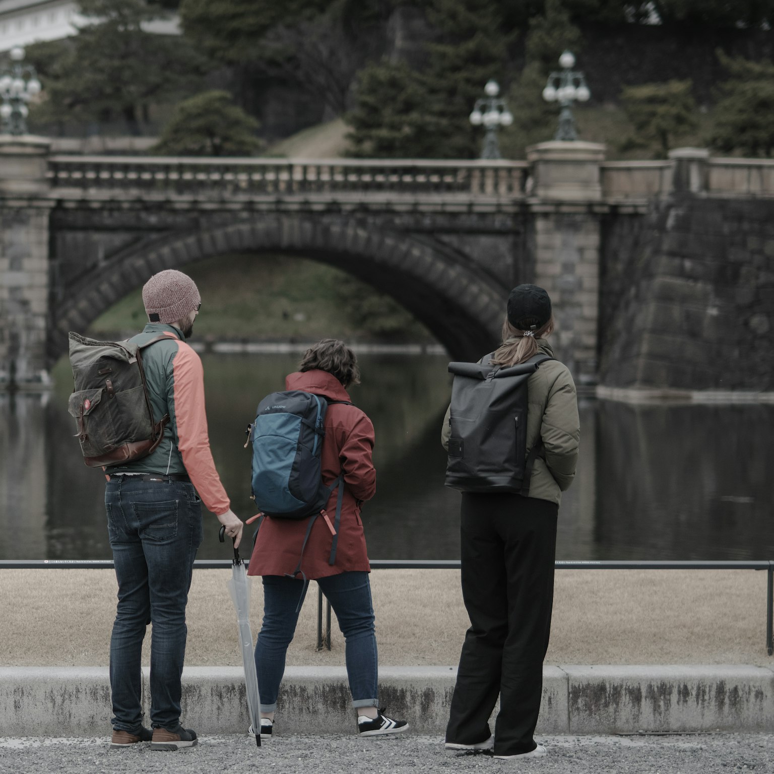 Three travelers looking at a bridge and pond