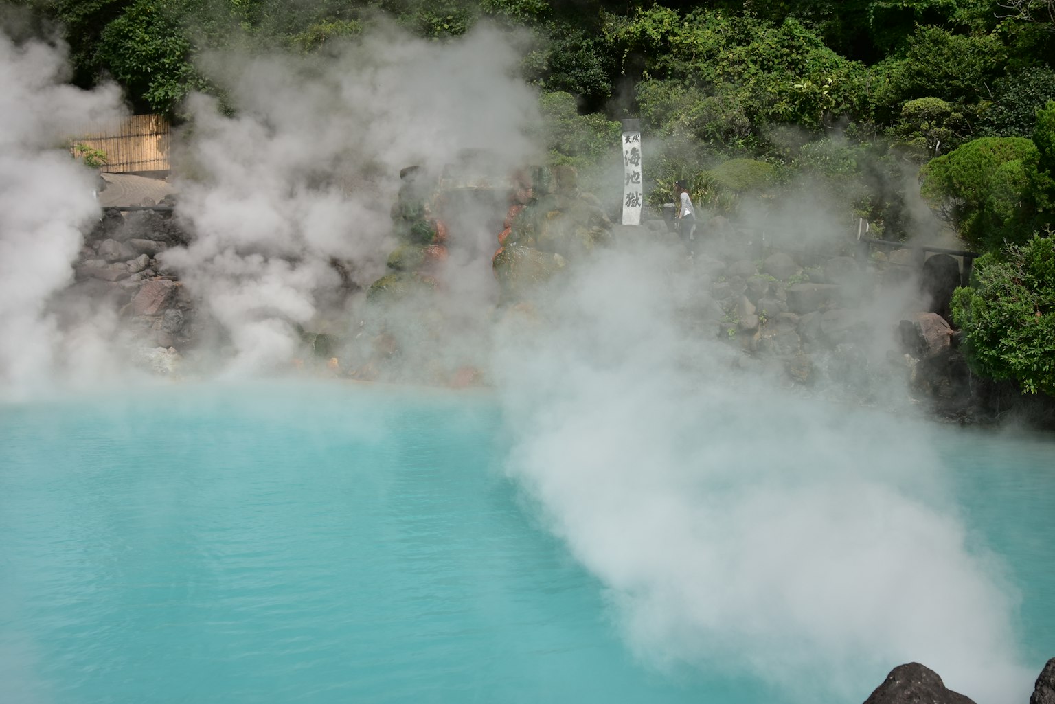 Pemandangan indah dari sumber air panas biru dikelilingi uap dan vegetasi subur
