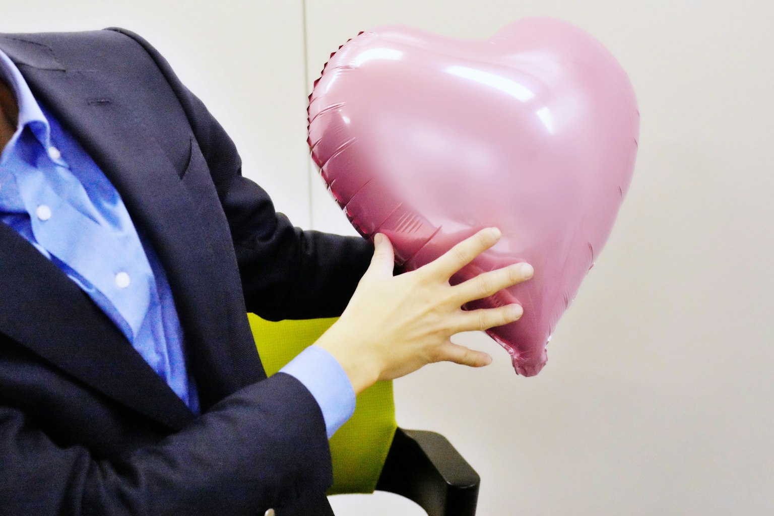 Tangan pria memegang balon berbentuk hati berwarna pink