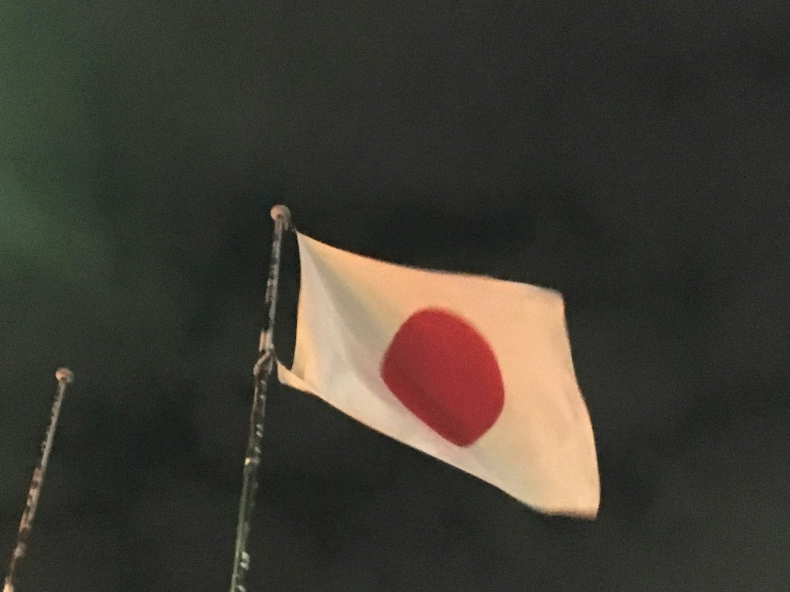 Bendera Jepang berkibar di langit malam dengan lingkaran merah di latar belakang putih