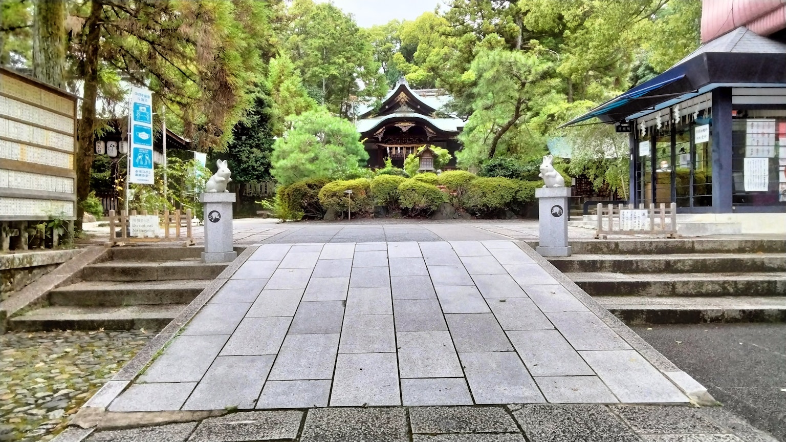 Quiet garden entrance with stone statues on both sides and a shrine in the background