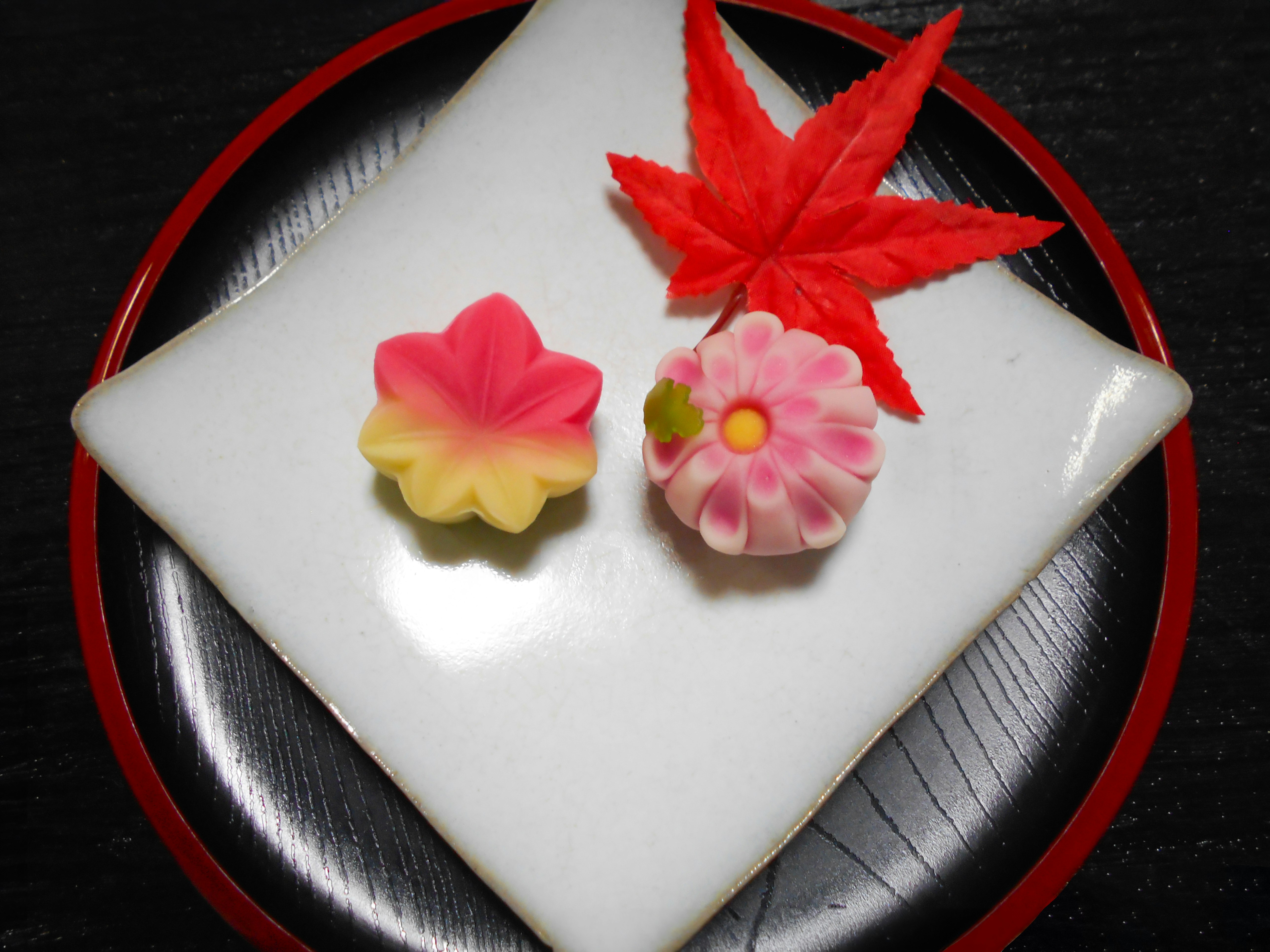 赤い花の和菓子と色とりどりの菓子が並ぶ白い皿