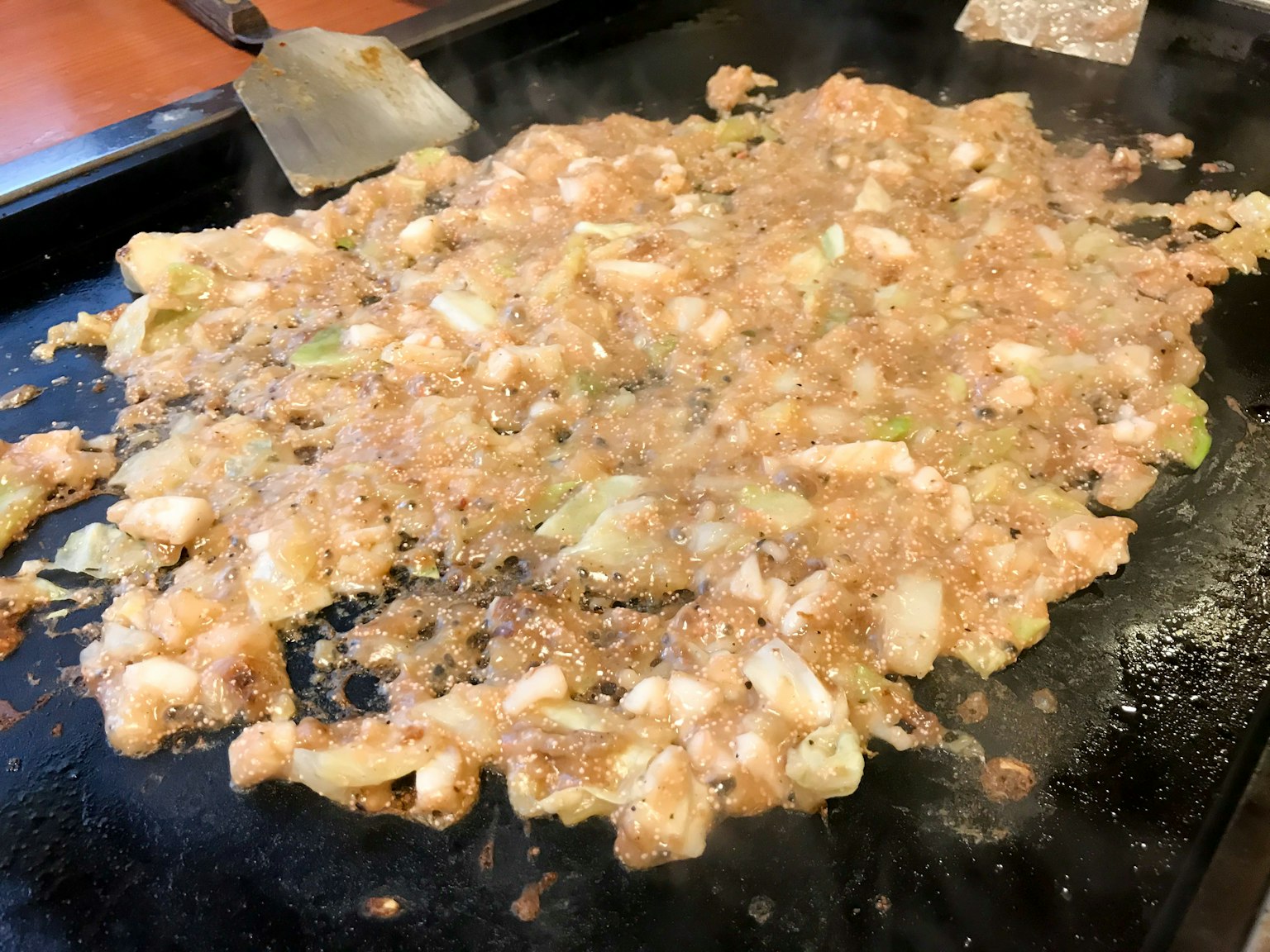 Partie d'okonomiyaki cuisinée sur une plaque avec des ingrédients mélangés