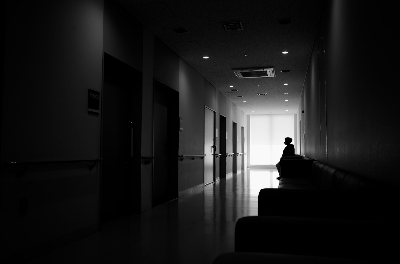 Silhouette d'une personne assise dans un couloir sombre avec une sortie lumineuse