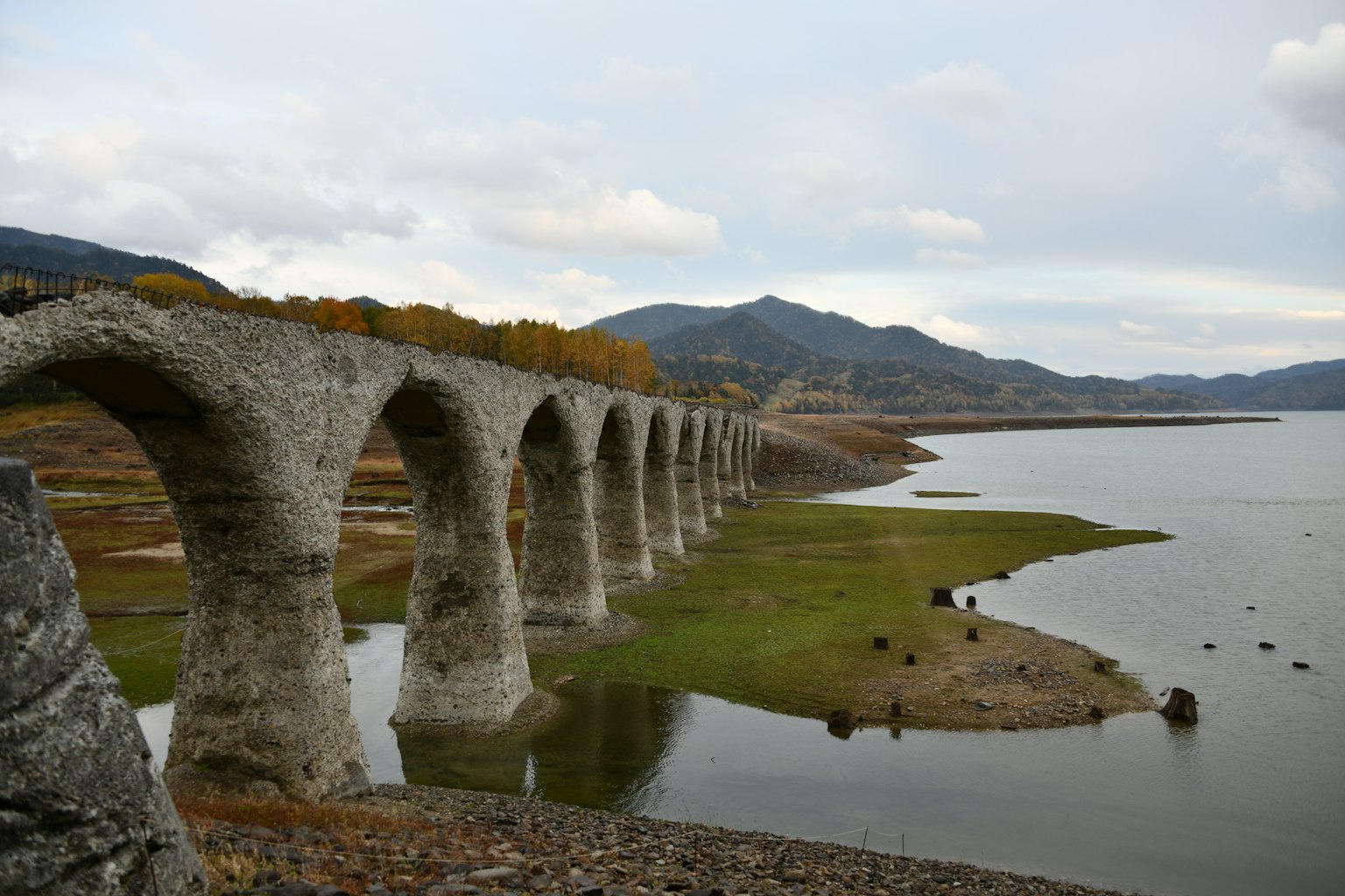Ancient stone aqueduct near a lake with mountains in the background