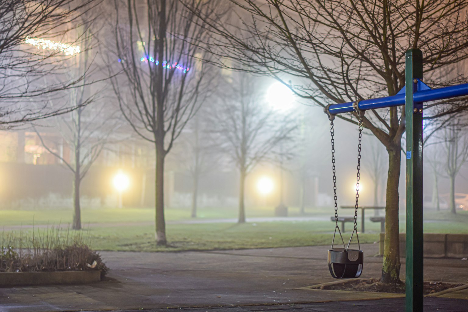 Taman dengan ayunan biru dan lampu di dalam kabut