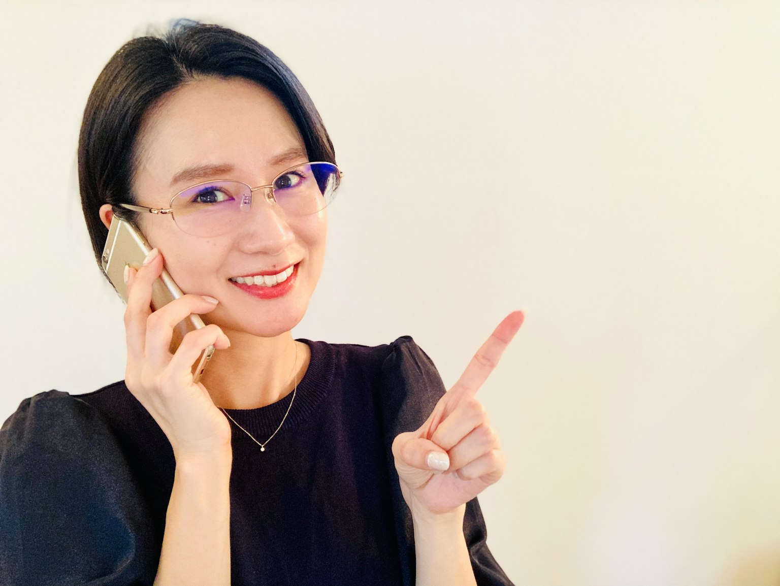 Wanita tersenyum saat berbicara di telepon sambil menunjuk jari