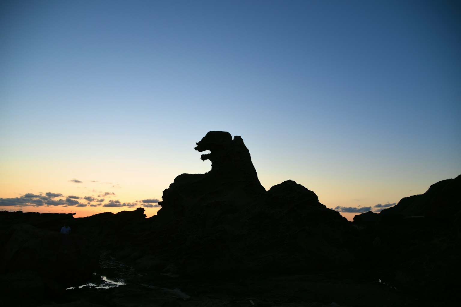 Silhouette of a rock formation resembling a beast against a sunset sky