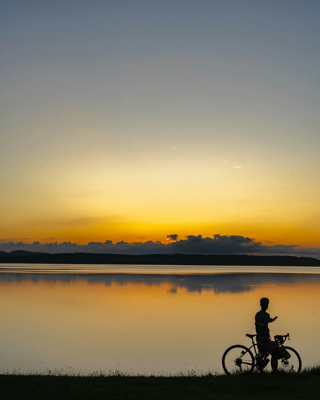 夕焼けの湖畔で自転車を押すシルエット