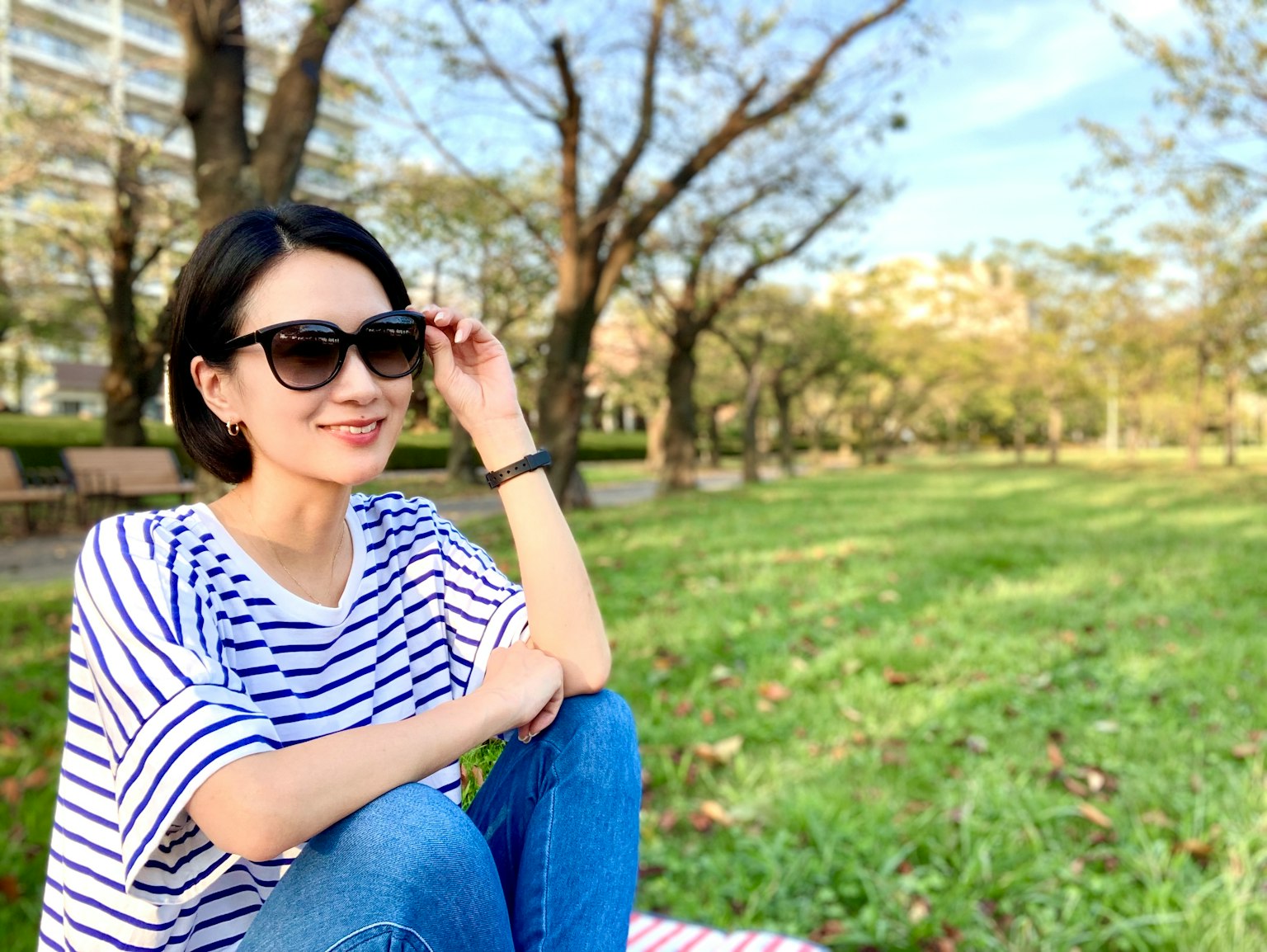 一位戴着太阳镜的女性坐在公园里，周围有树和草