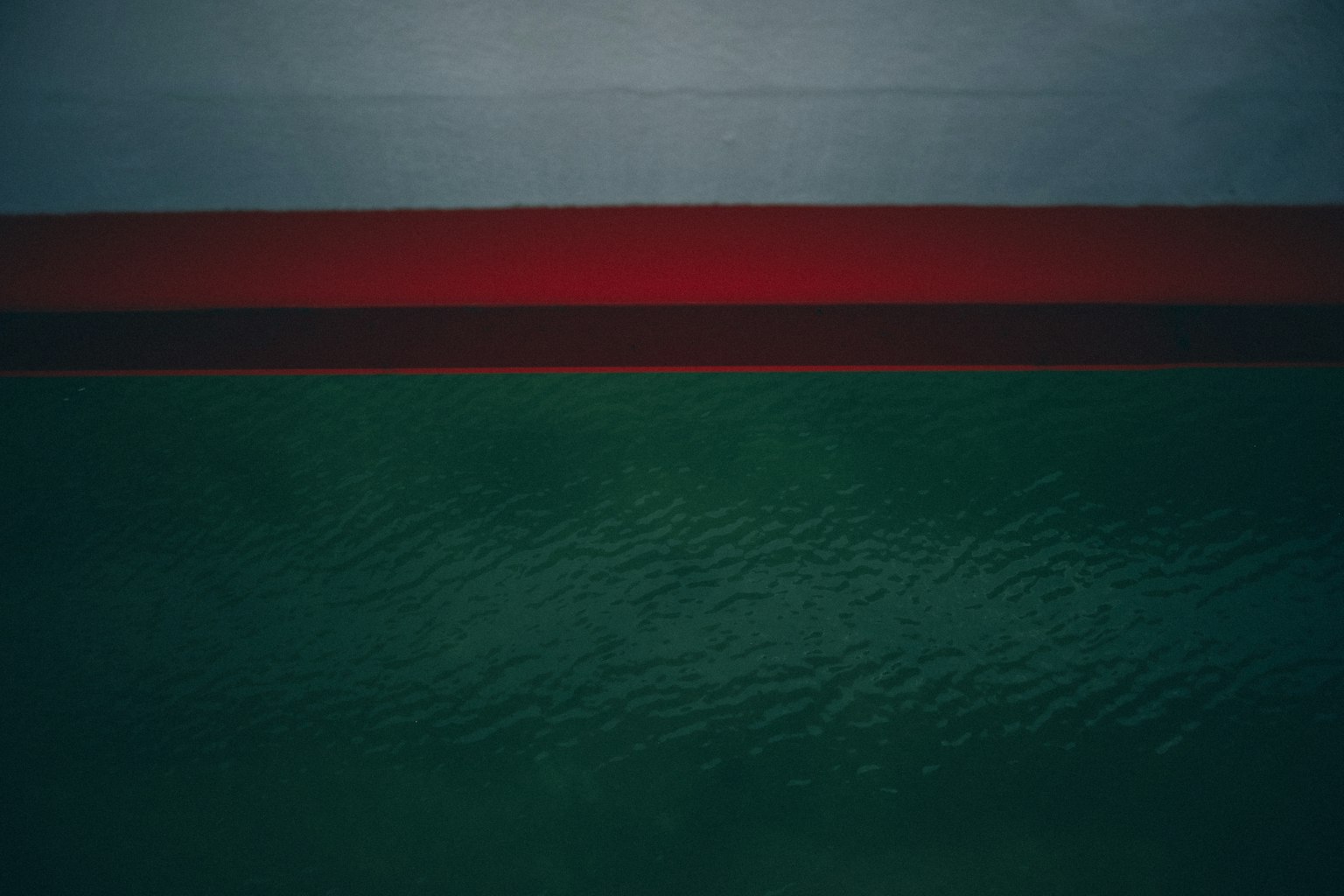 Costado de barco con agua azul y franja roja