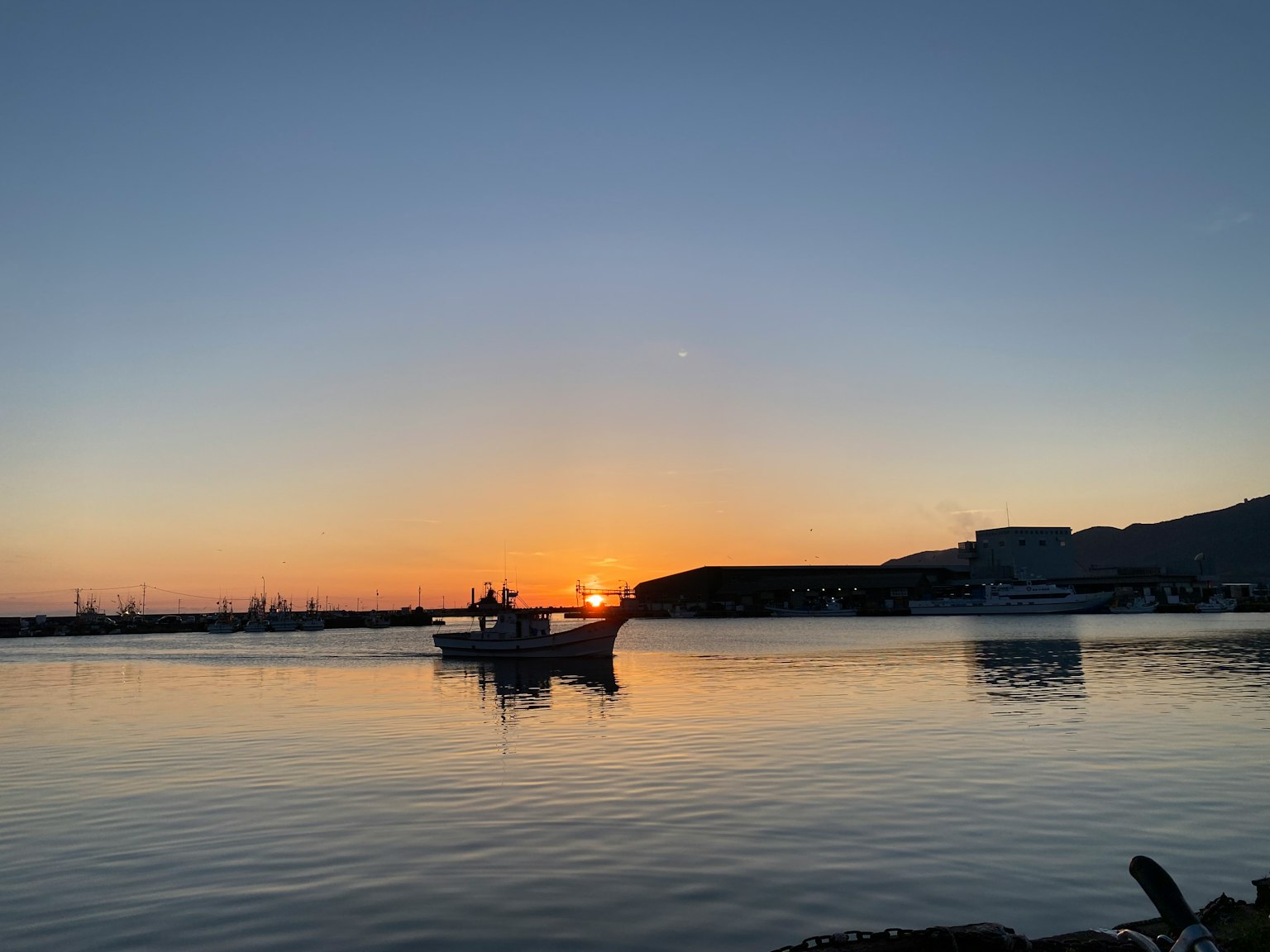 A tranquil harbor scene with a small fishing boat silhouetted against the sunset