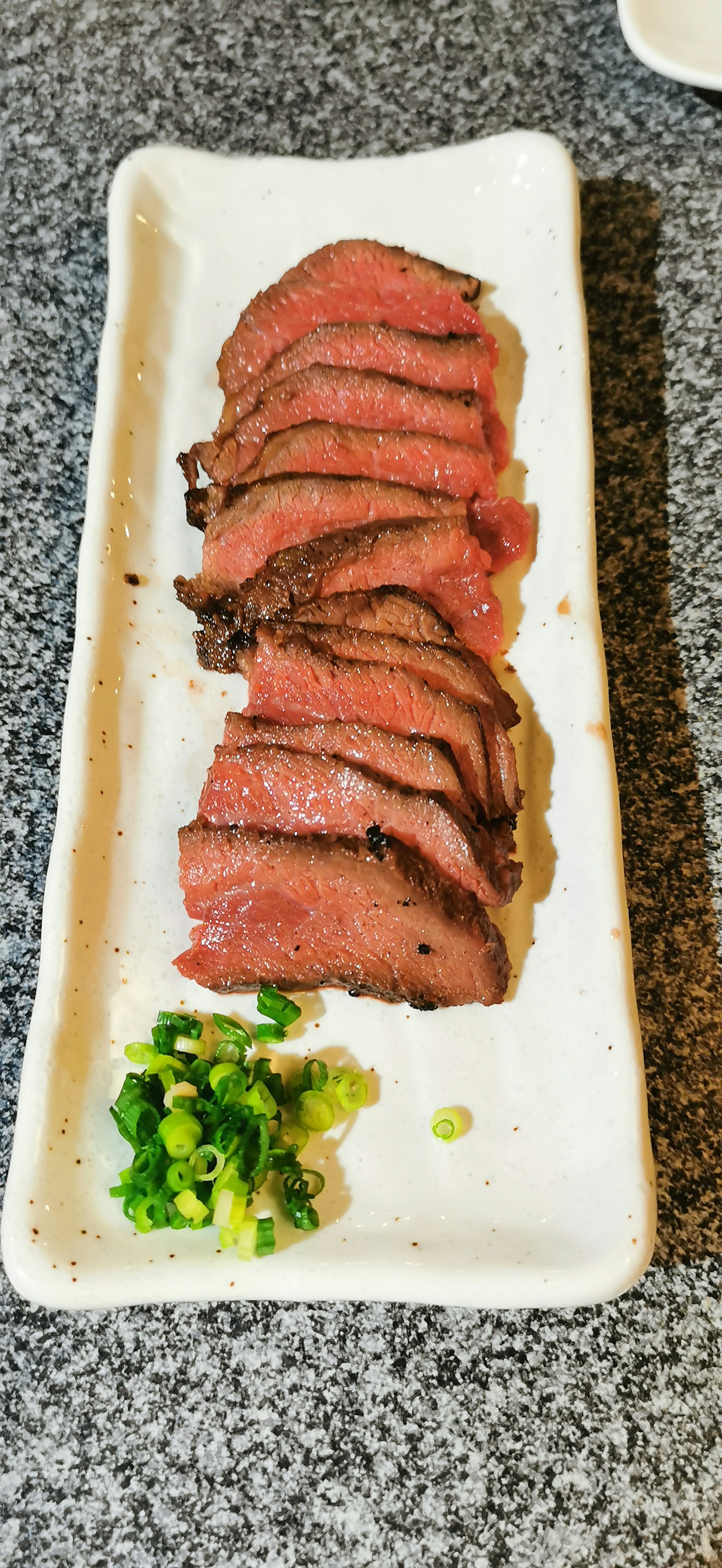Rodajas de carne asada en un plato blanco con cebollitas verdes picadas