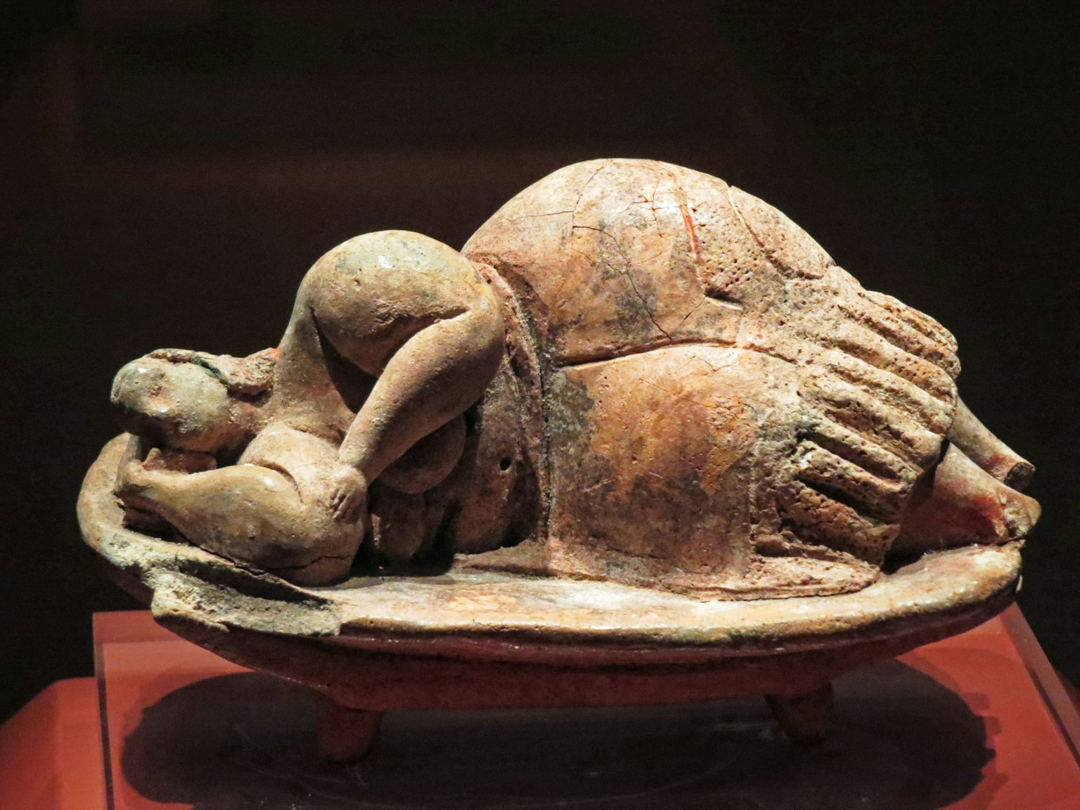 Antike Skulptur, die eine menschliche Figur zeigt, die sich neben einem gefälschten Schildkrötengefäß zusammenrollt