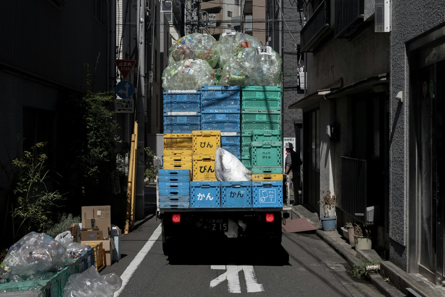 Camion de collecte des déchets chargé de conteneurs en plastique bleus dans une ruelle étroite