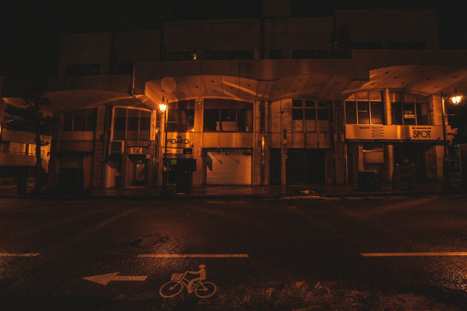 Extérieur de bâtiments dans une rue sombre avec des lampadaires et un symbole de vélo