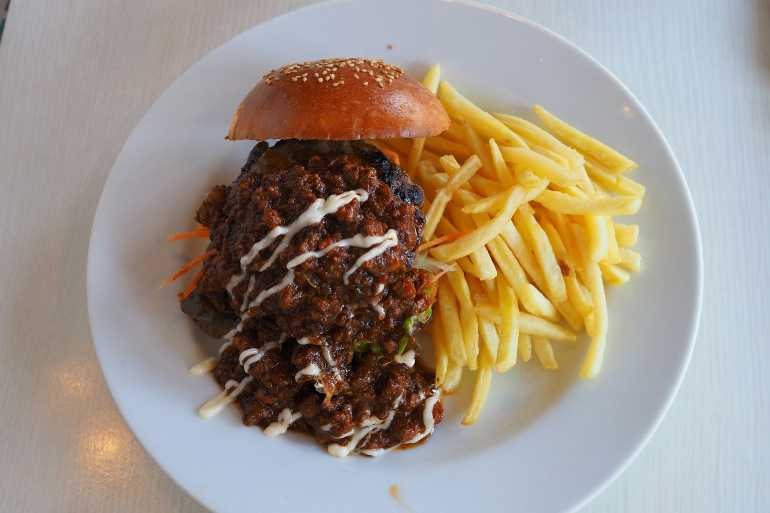 A plate featuring a hearty hamburger topped with shredded vegetables and a side of crispy fries