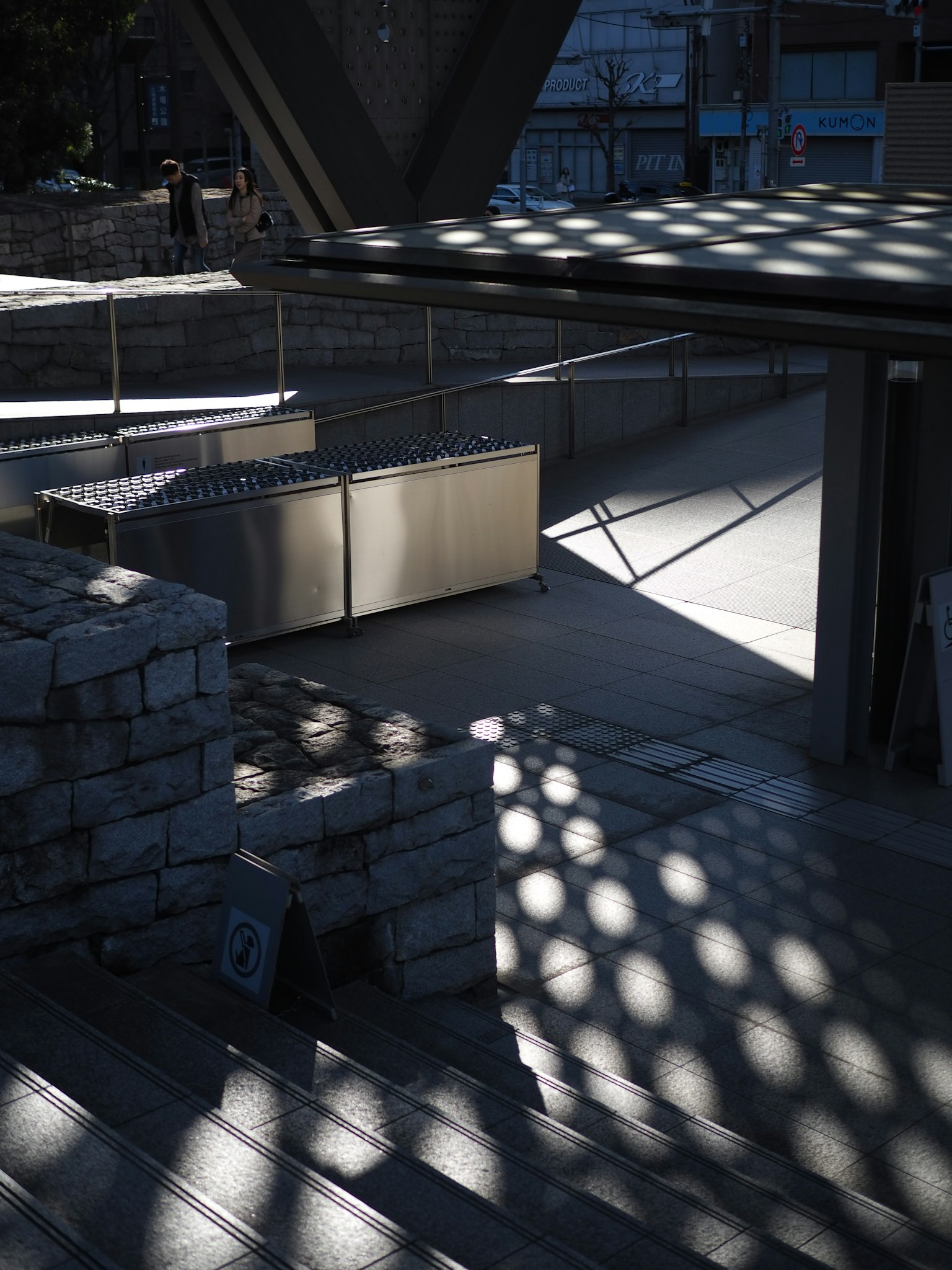 Área al aire libre con mesas metálicas y sombras impactantes en las escaleras