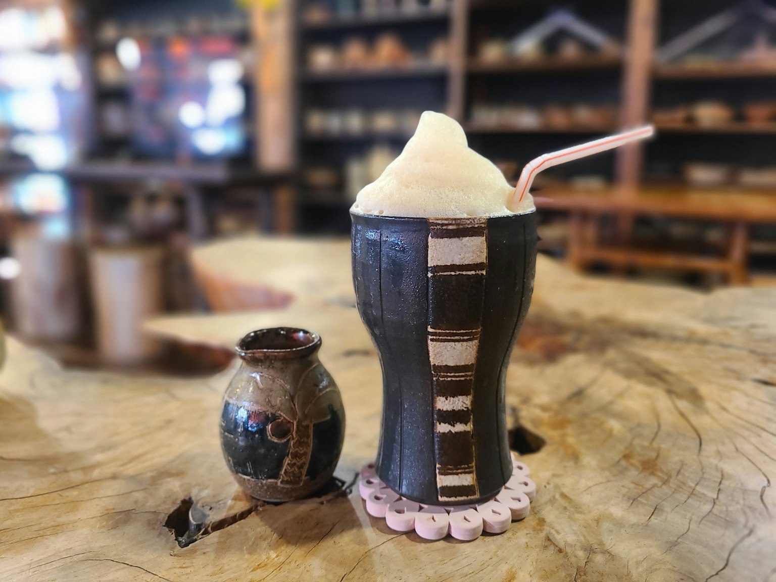 A ceramic cup with a float drink and a small clay pot beside it