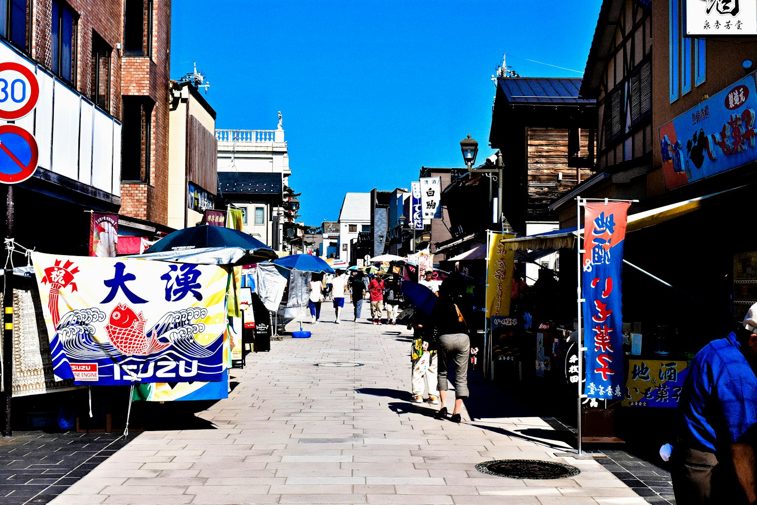 붐비는 시장 거리에서 사람들이 걷고 있고 다채로운 노점이 늘어서 있는 모습