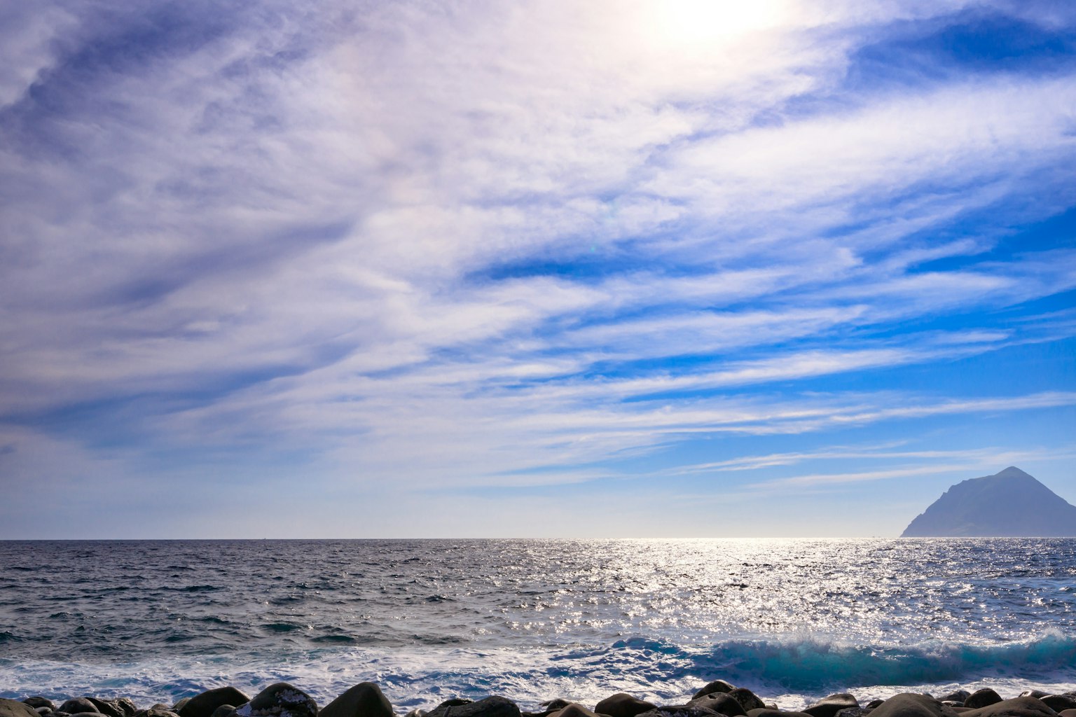 Scenic view of blue skies and ocean with gentle waves and distant mountain