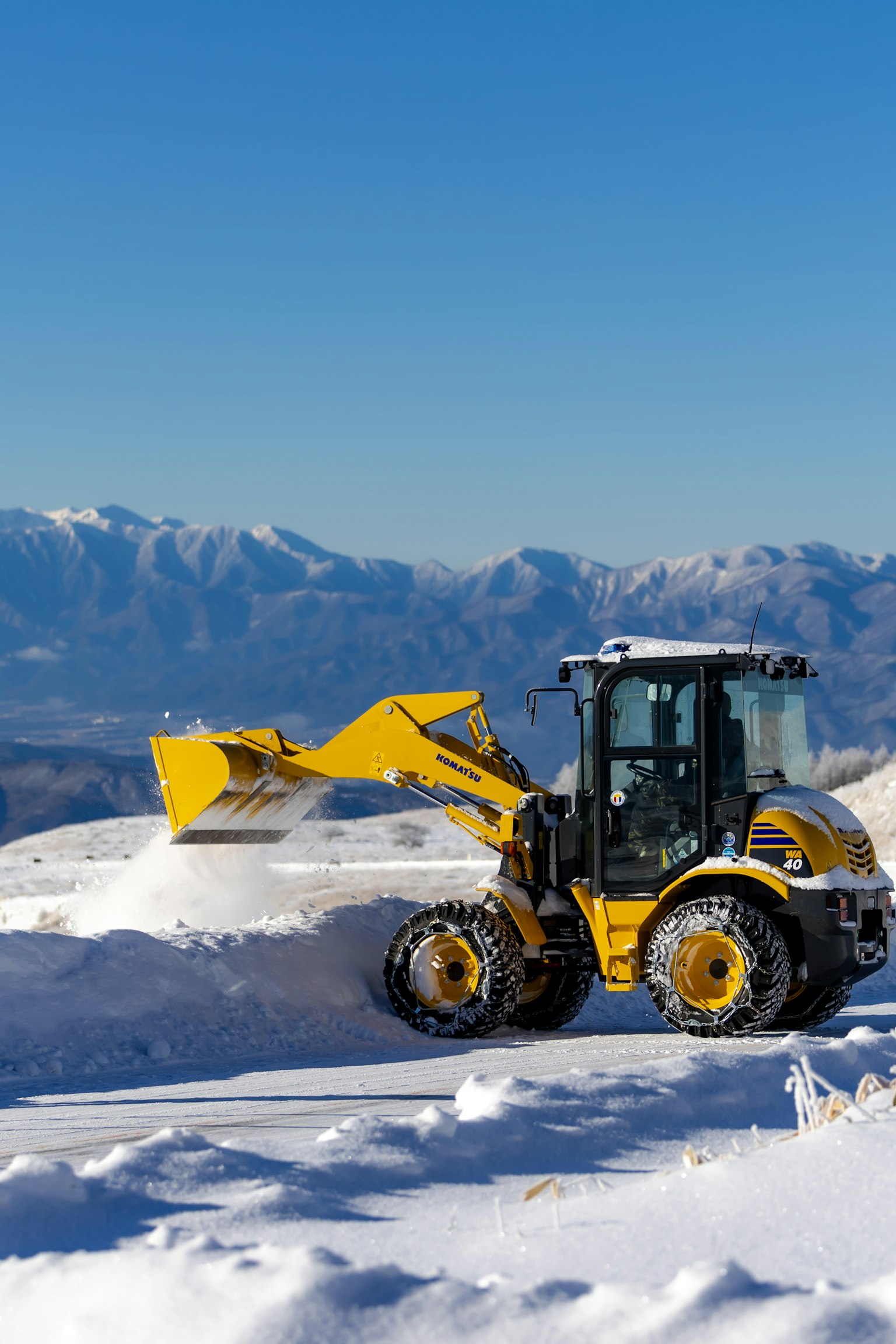 Gelber Bagger arbeitet im Schnee mit Bergkulisse