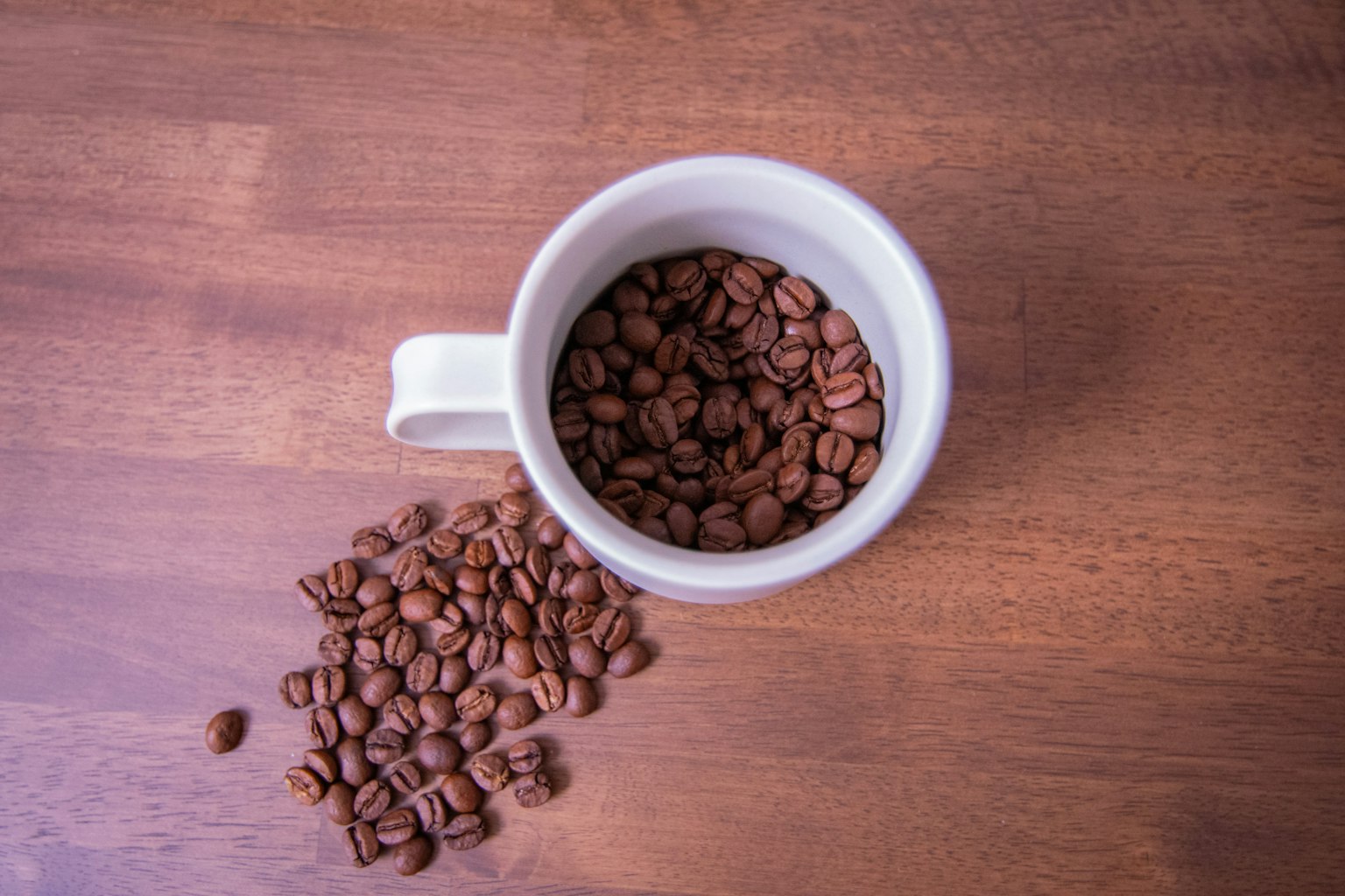 Cangkir putih berisi biji kopi di atas meja kayu