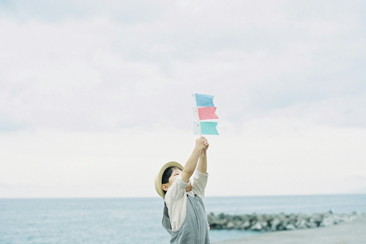 Anak memegang bendera berwarna-warni di pantai