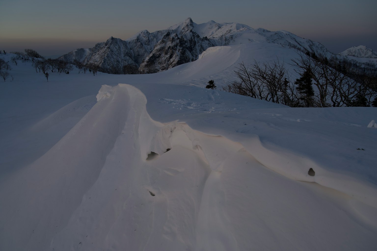 Paisaje montañoso cubierto de nieve con ondulaciones en el crepúsculo