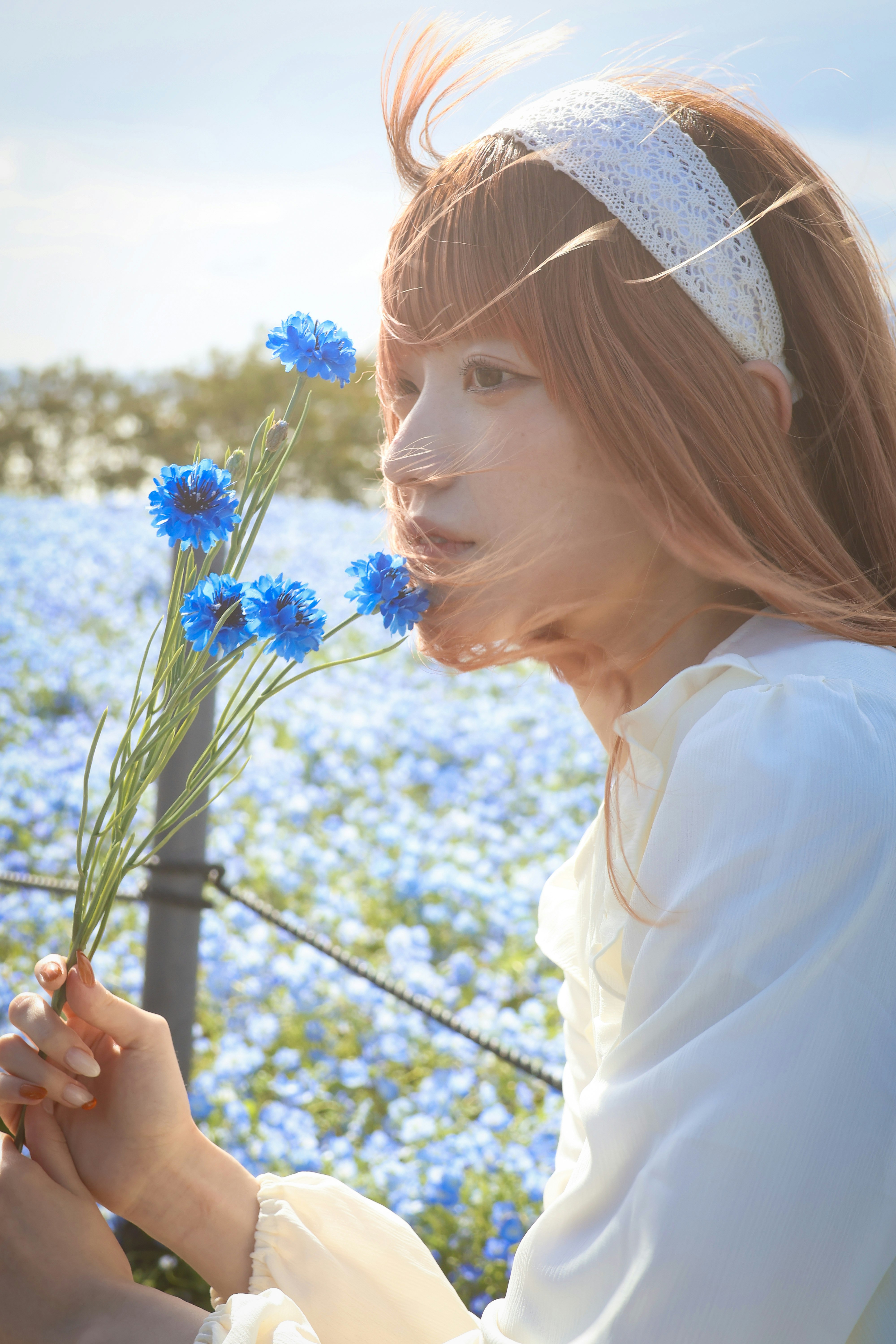 ผู้หญิงยิ้มมองด้านข้างถือดอกไม้สีฟ้าใต้ท้องฟ้าโปร่งใส