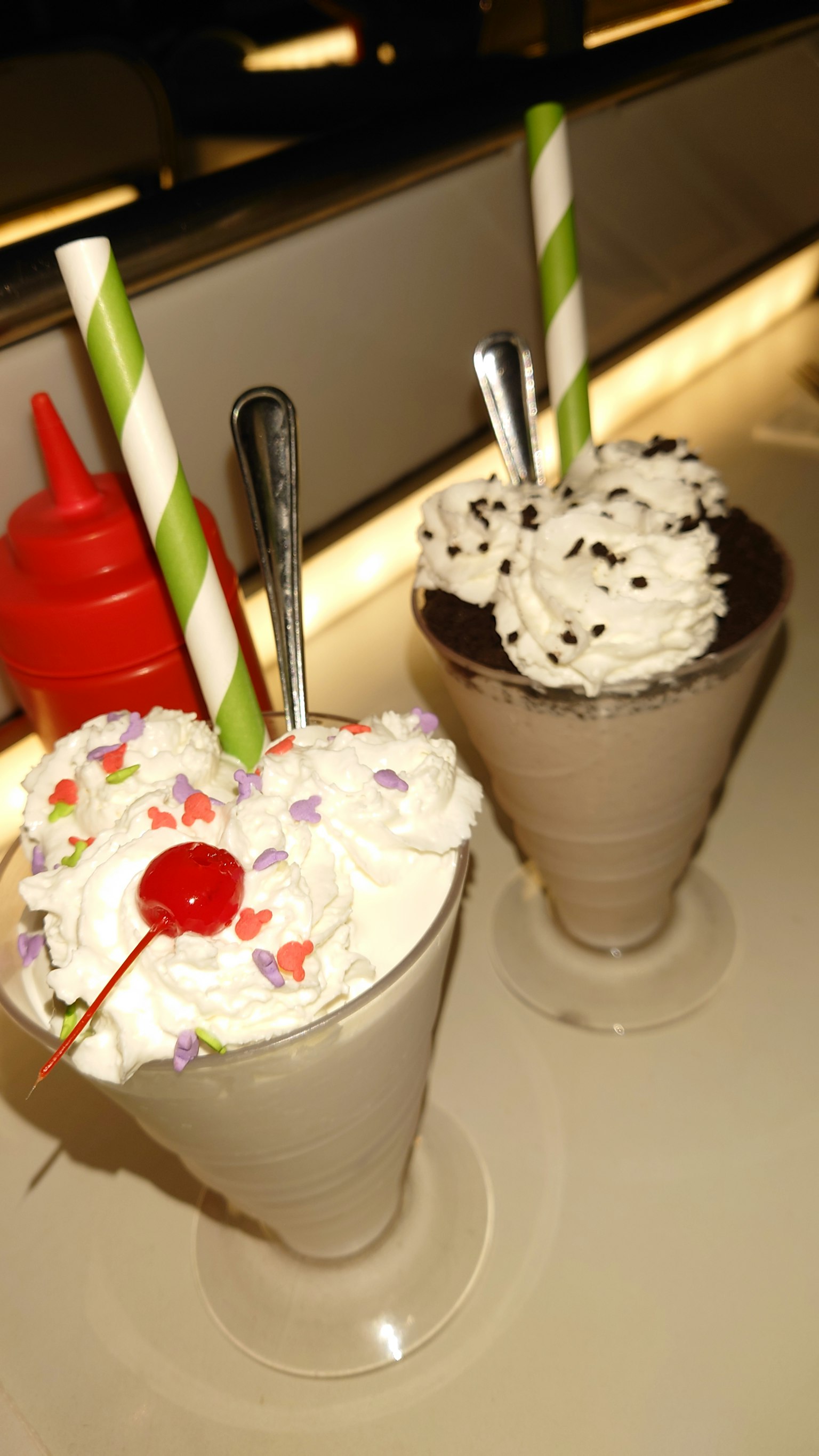 Due frullati di gelato serviti in bicchieri con panna montata e una ciliegia su uno decorato con sprinkles colorati