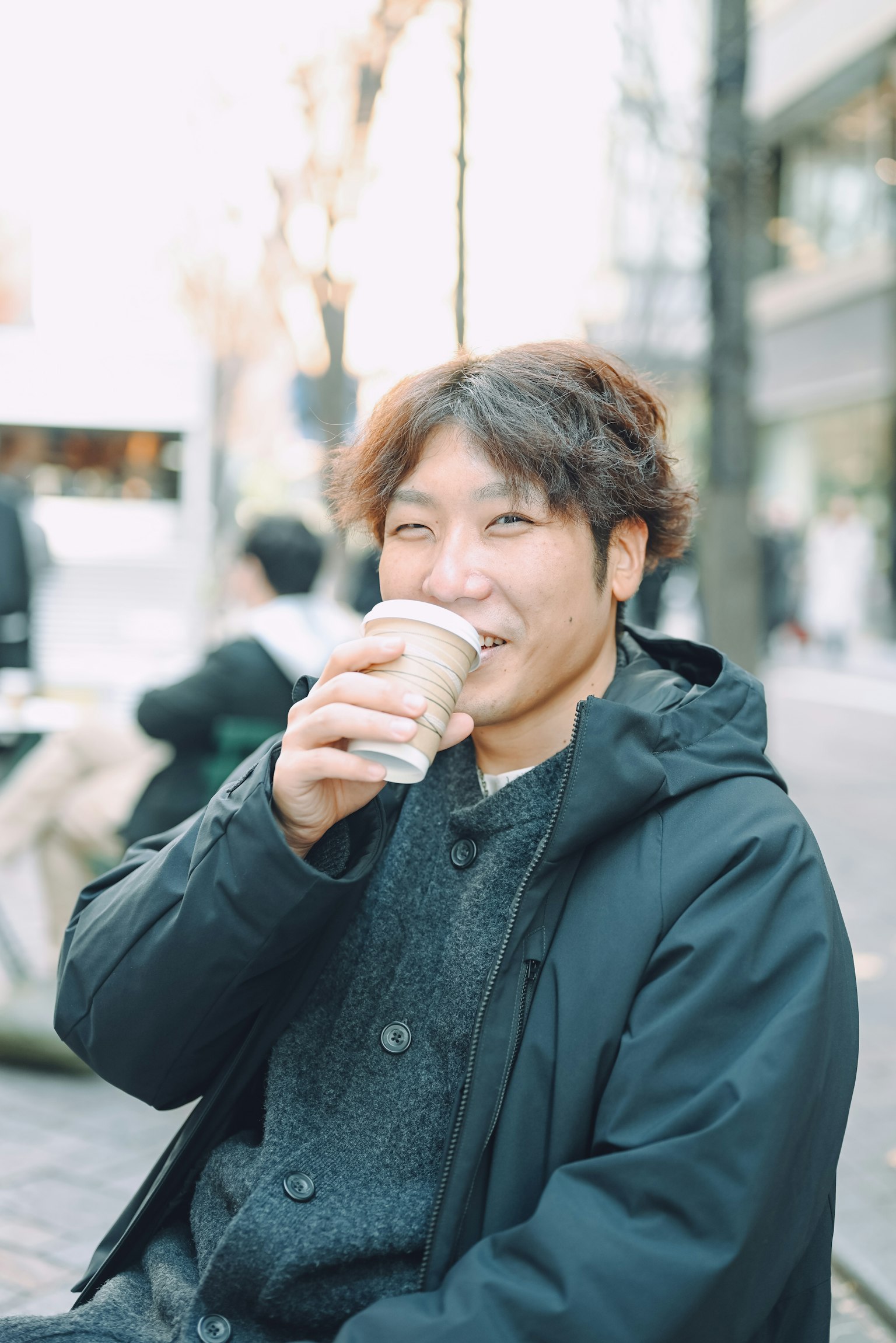 ชายยิ้มดื่มกาแฟในสภาพแวดล้อมในเมือง