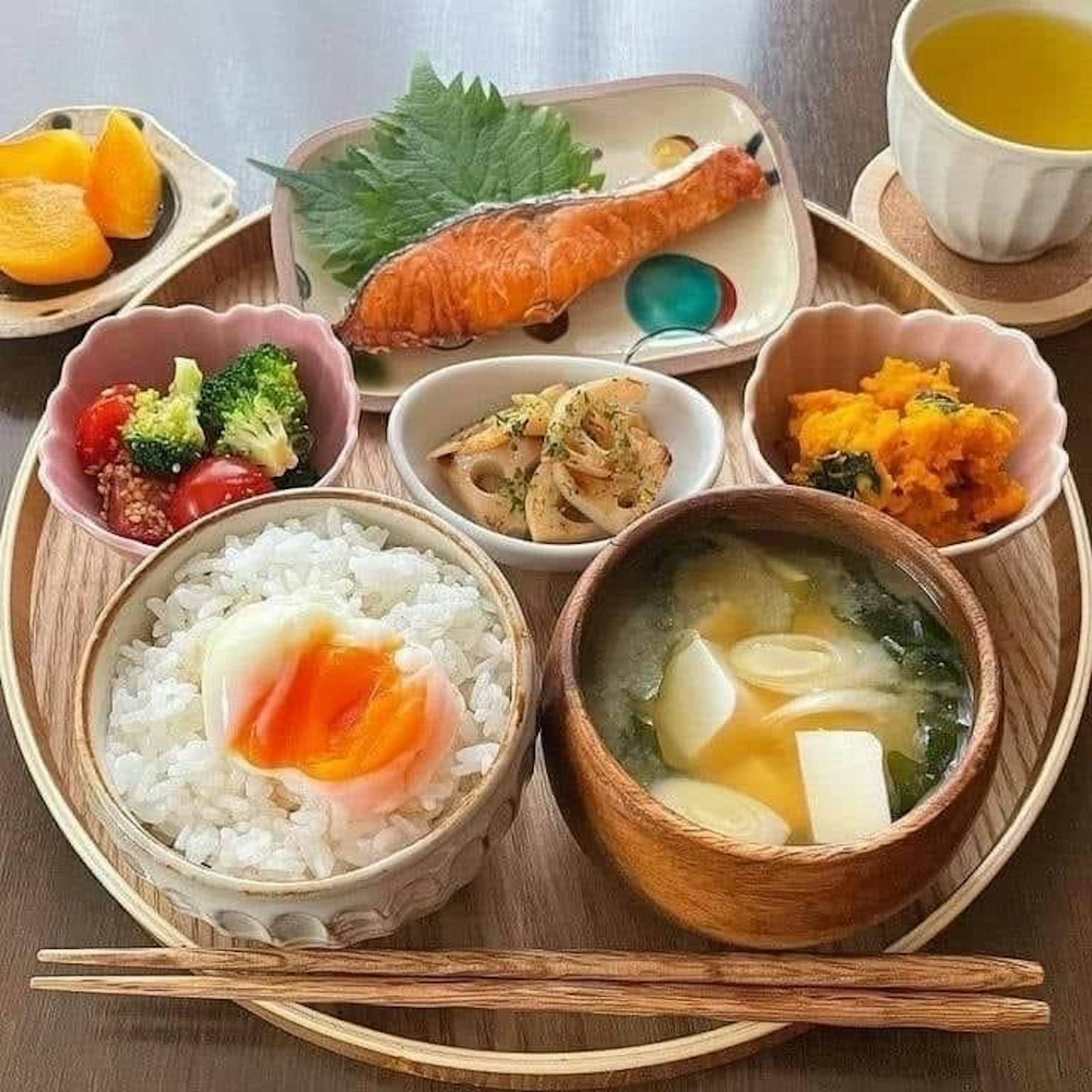 Un delizioso piatto di colazione giapponese con riso, zuppa di miso, salmone grigliato, contorni vegetali, un uovo e tè