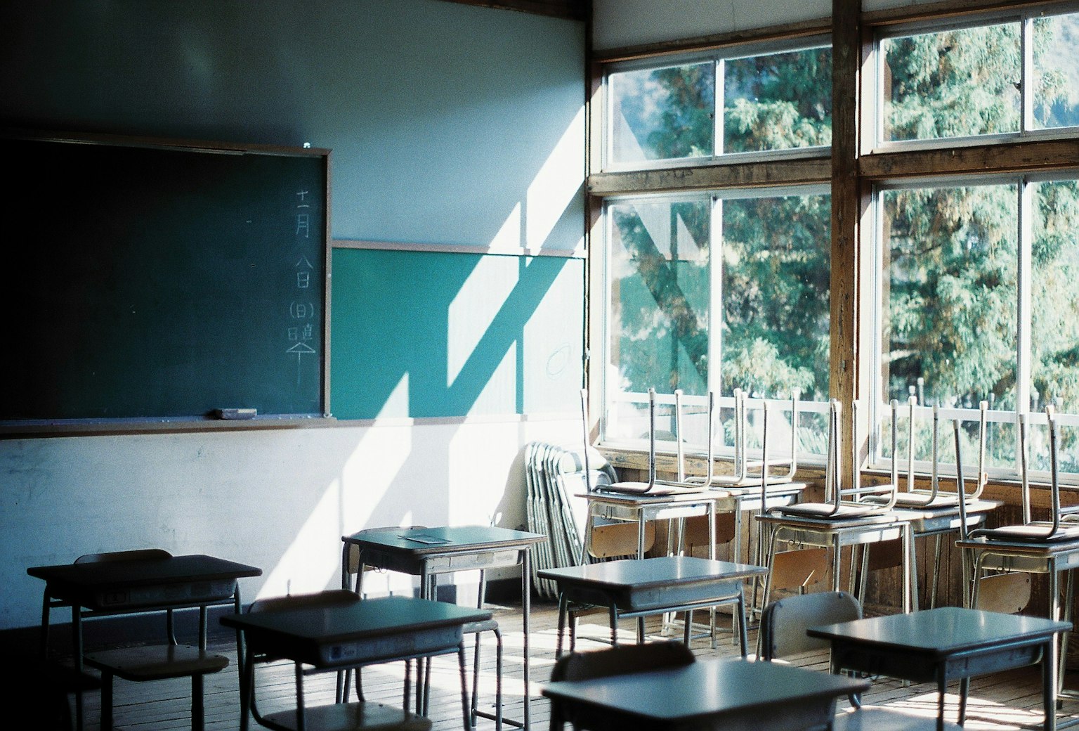 Interior de un aula con escritorios y sillas dispuestos luz natural que entra por las ventanas