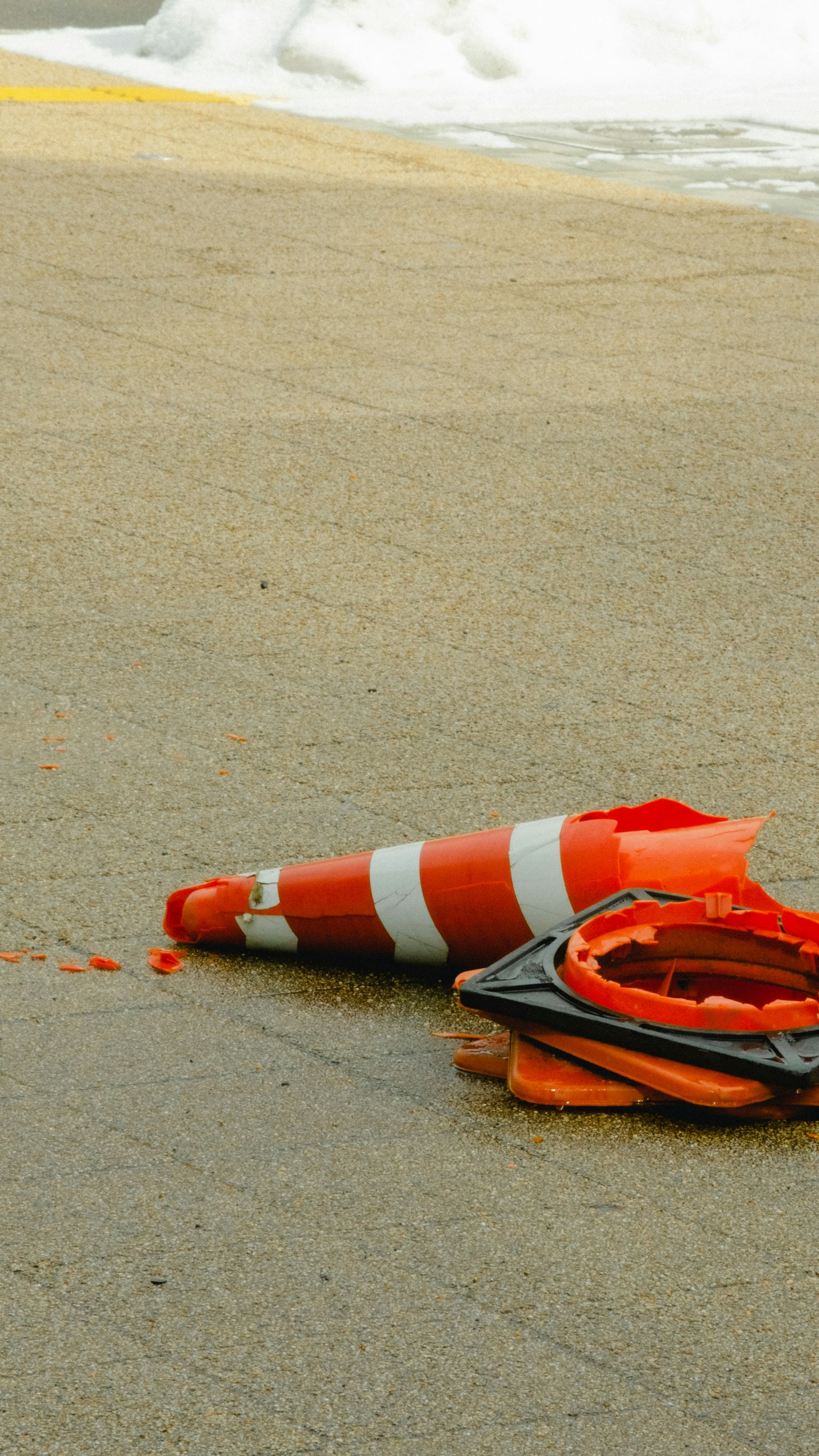Un cono de tráfico naranja caído con franjas blancas en el suelo cerca de nieve